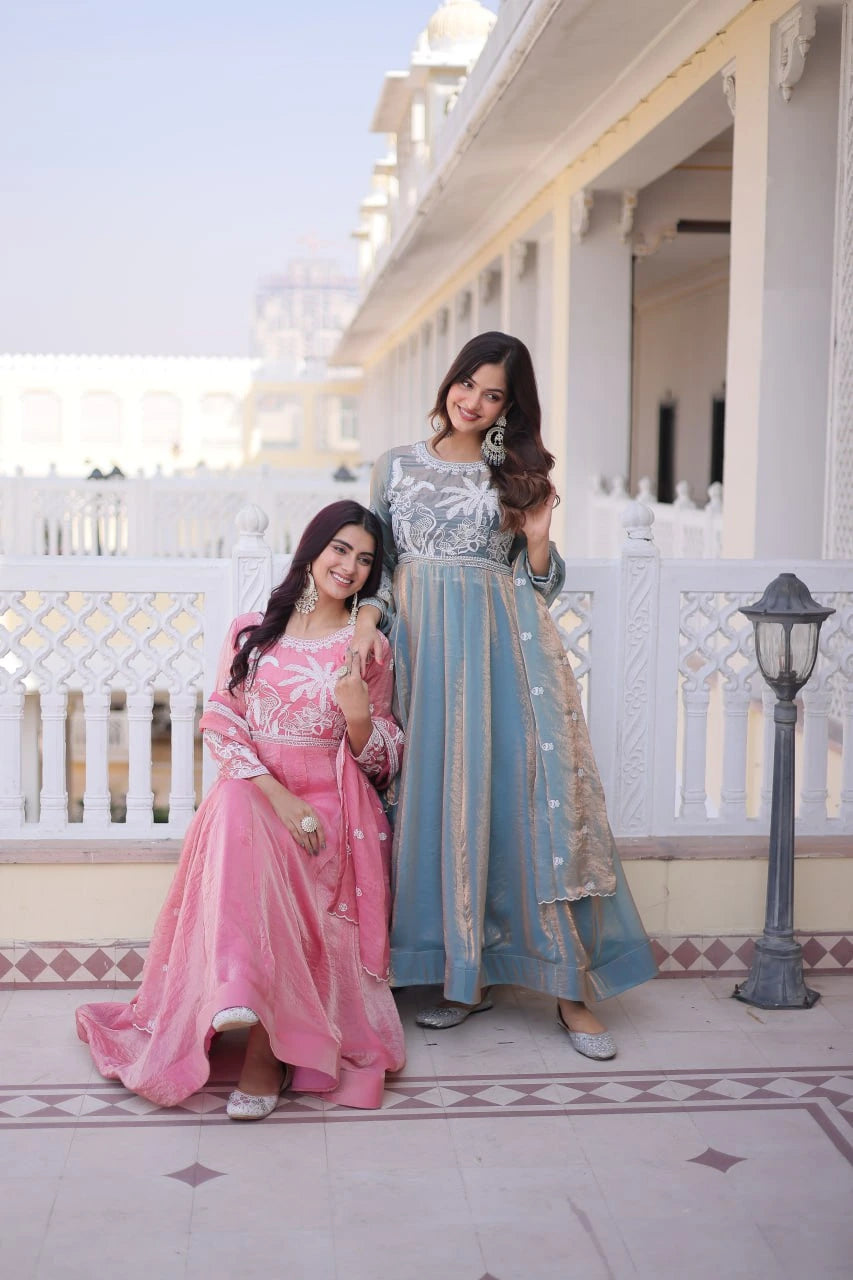 Two women in traditional outfits standing on a balcony with a building in the background.